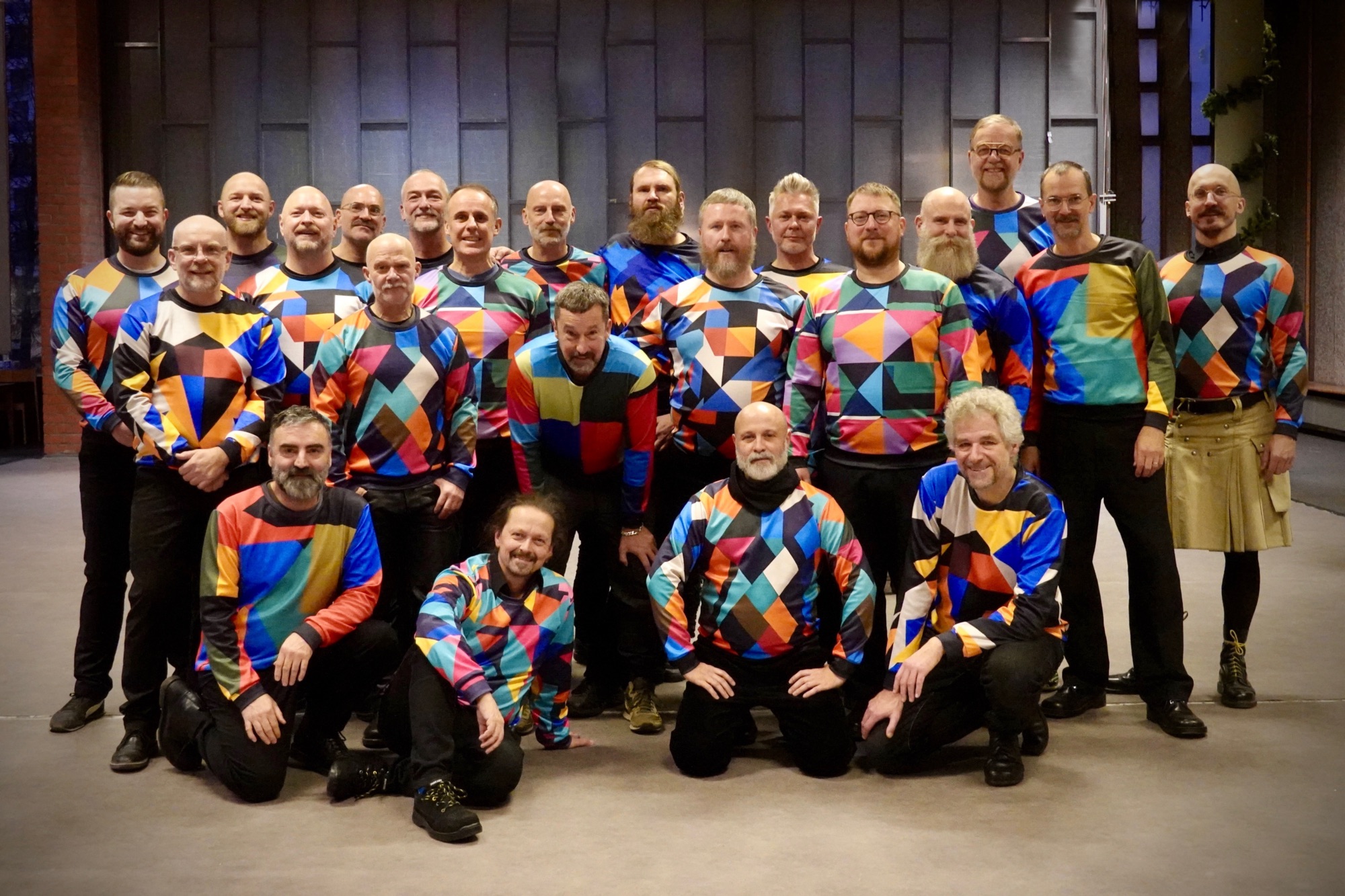 Pet Shop Bears Chorfoto. 20 Sänger mit bunten Shirts und schwarzen Hosen.